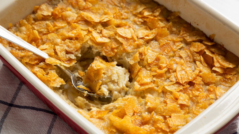 Enamel baking dish filled with funeral potatoes, with part of the potatoes scooped out with a spoon