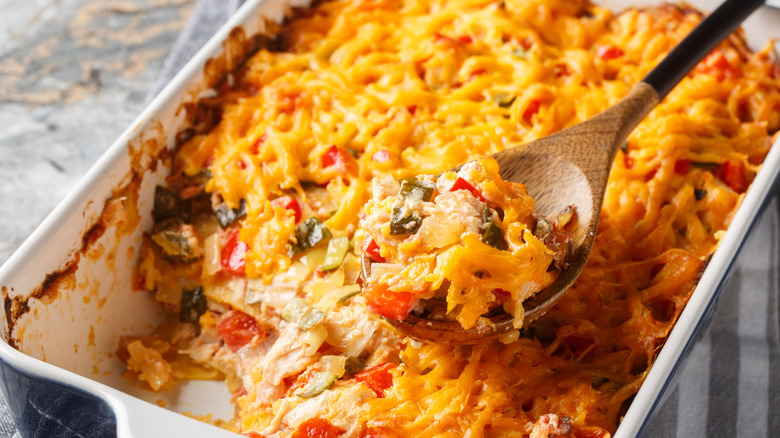 A baking pan filled with King Ranch chicken casserole, with some scooped out with a wooden spoon