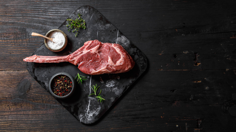 raw cowboy steak on marble slab with various seasonings