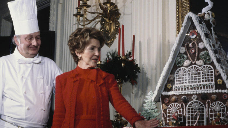 White House chef with Nancy Reagan, in red, gesturing toward ornate gingerbread house