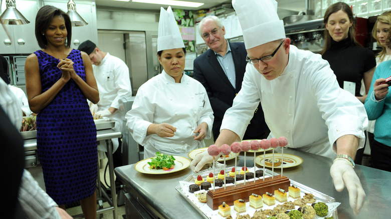 White House chef displays a tray of brightly-colored pastries to Michelle Obama as others look on in the kitchen