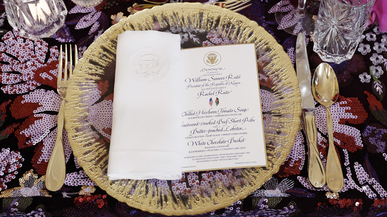 Place setting and menu for White House state dinner for Kenyan president on floral tablecloth with gold flatware