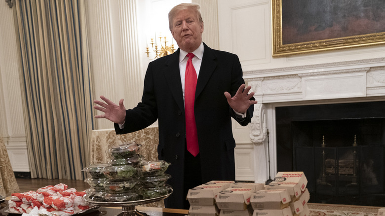 Trump in red tie gestures to a table full of fast food laid out
