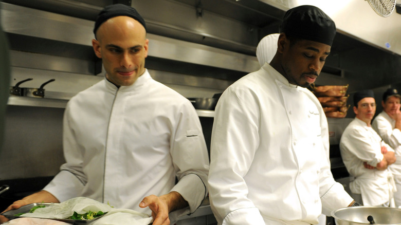 White House Chef Sam Kass, carrying a tray, keeps an eye on sous chef