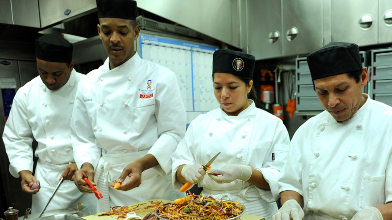 Four diverse White House chefs concentrate on peeling carrots and radishes in the kitchen