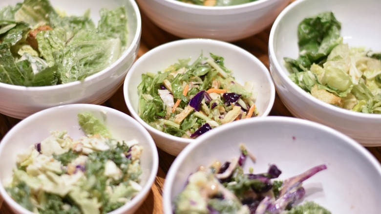 A collection of white bowls with various salads in them