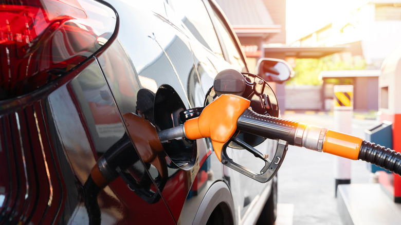Orange gas pump inserted into the gas compartment on a black SUV.