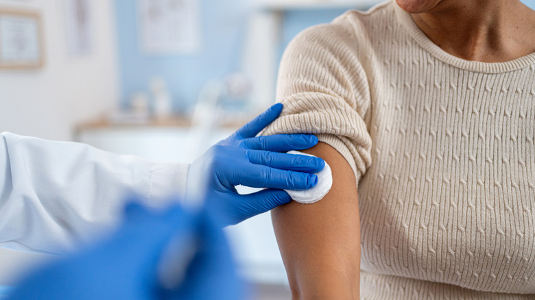 Up-close image of a woman receiving a shot from a person in blue medical gloves.