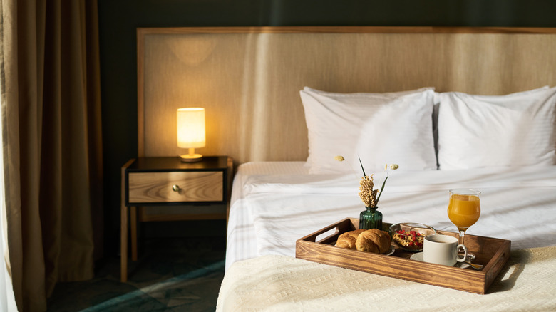 A hotel bed with a tray of breakfast foods and orange juice