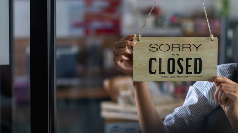 Person hanging a "closed" sign on restaurant door
