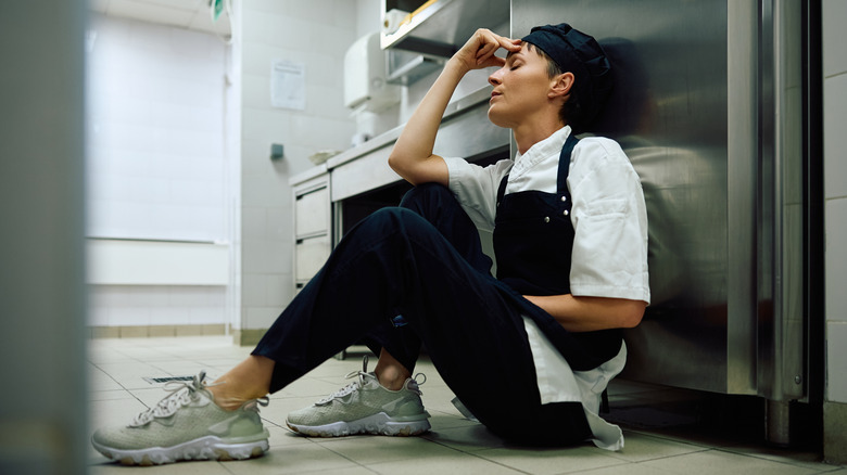 Frustrated restaurant worker sitting on kitchen floor