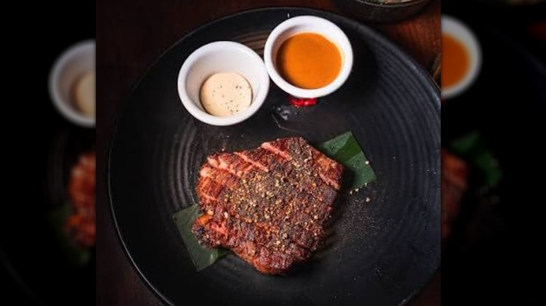 Steak on a black plate with sauces in bowls