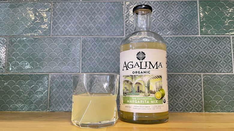 Bottle and glass of Agalima Organic Authentic Margarita Mix on a wooden counter top