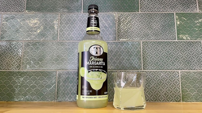 Bottle and glass of Mr. & Mrs. T Skinny Margarita Mix on a wooden counter top
