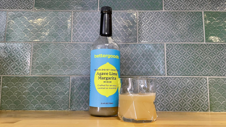 Bottle and glass of Bettergoods Agave Lime Margarita Mixer on a wooden counter top
