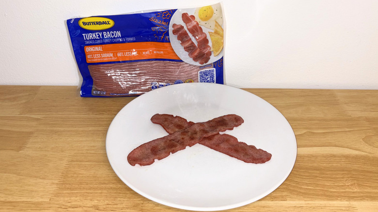 Two pieces of Butterball turkey bacon laid across each other on a white plate with the package behind it.