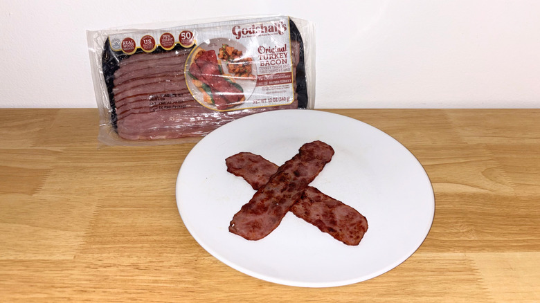 Two pieces of Godshall's turkey bacon laid across each other on a white plate with the package behind it.