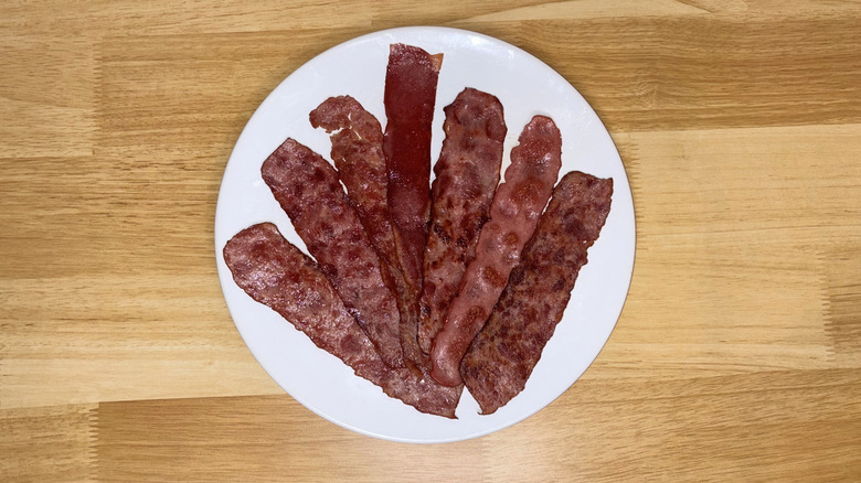 Seven pieces of turkey bacon laid out on a white plate on a wood countertop.