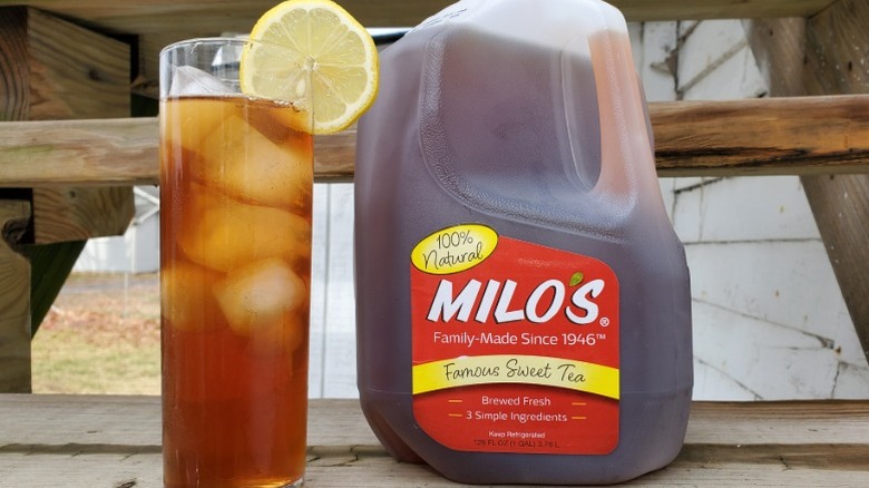 A gallon of Milo's sweet tea next to a tall glass of tea with ice and a slice of lemon