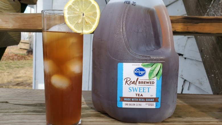 A gallon of Kroger sweet tea next to a tall glass of tea with ice and a slice of lemon