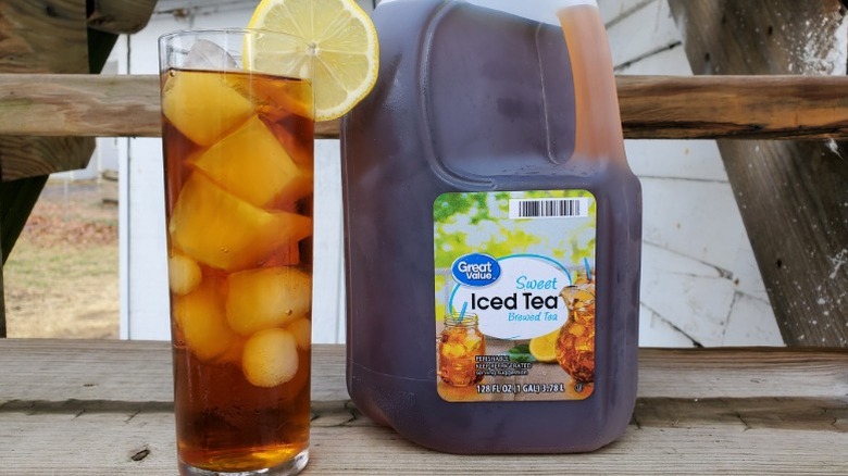 A gallon of Great Value sweet tea next to a tall glass of tea with ice and a slice of lemon