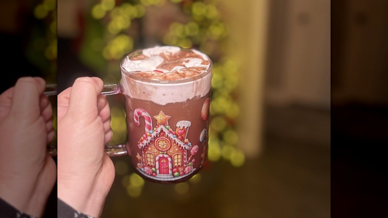 Hand holding a mug of hot chocolate topped with marshmallow fluff