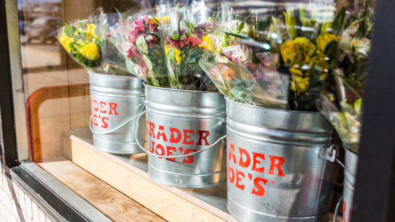 Three silver pails full of bouquets of flowers in a window of a Trader Joe's grocery store