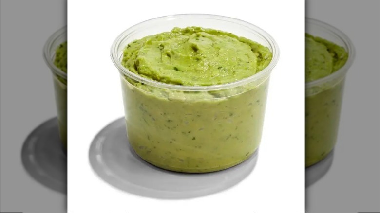 Guacamole in a wooden bowl next to halved avocados and a wooden spoon