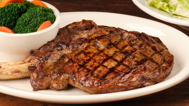 The bone-in ribeye steak with a side of vegetables on a white plate from Texas Roadhouse