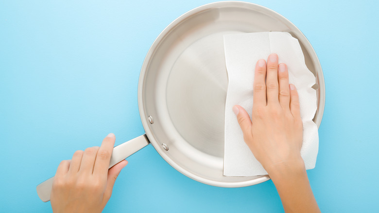 Person wiping stainless steel pan with paper towel