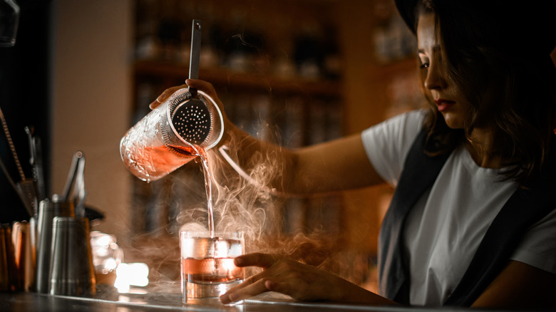 woman making an intricate cocktail with smoke
