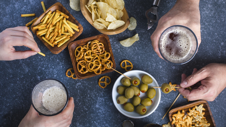 people holding beer glasses while munching on various snacks