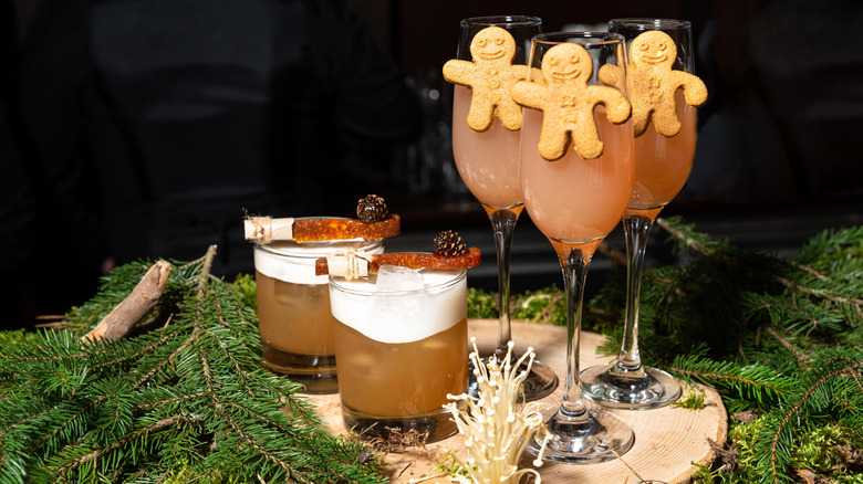two holiday themed cocktails on a wooden board with pine tree leaves