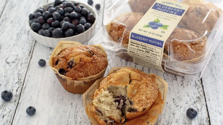 Trader Joe's blueberry muffins and a bowl of blueberries on a white wooden surface