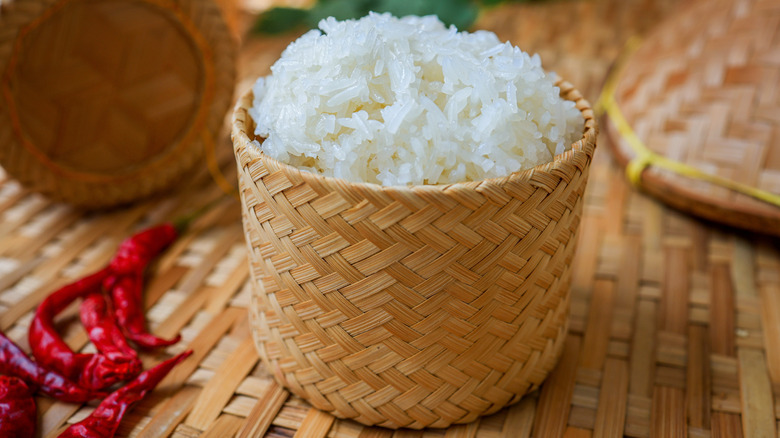 wooden basket with sticky rice next to a few red chili peppers