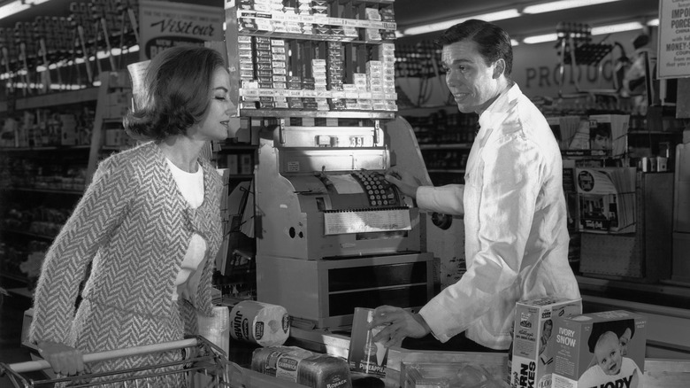 A black-and-white photo of a cashier typing item numbers into a cash register