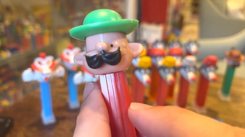 Closeup of a hand holding an Alpine Man PEZ dispenser, with other PEZ dispensers in the background