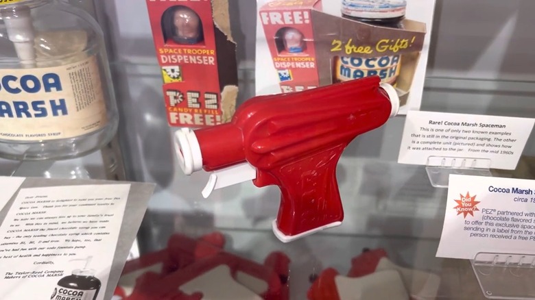 Red 1950's PEZ space gun on a display shelf with other PEZ artifacts