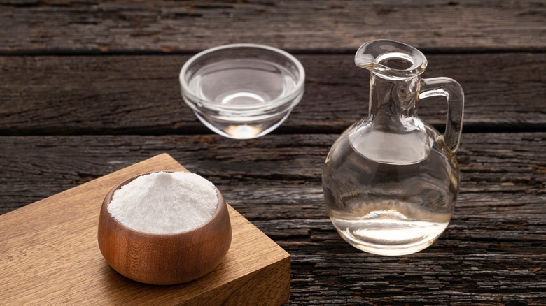 Baking soda in a wooden bowl and white vinegar in a glass jug