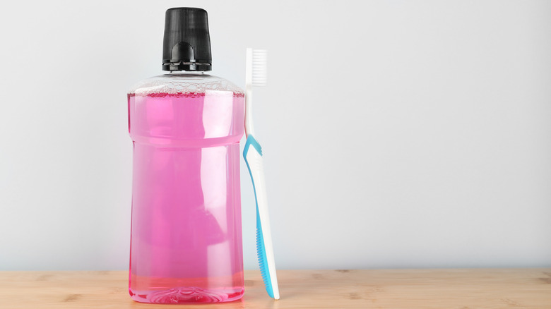 Bottle of pink mouthwash with toothbrush propped up against it