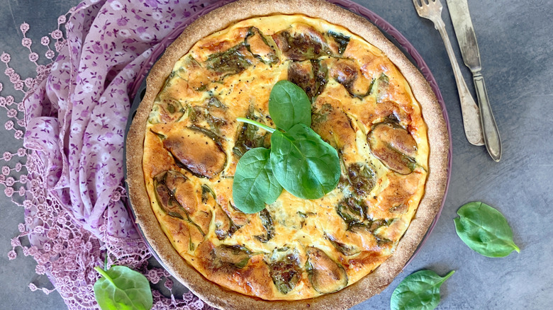 a cottage cheese quiche with spinach alongside a purple cloth on a marble background
