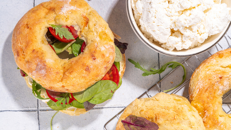 a bagel sandwhich made with cottage cheese and a bowl of cottage cheese in the background