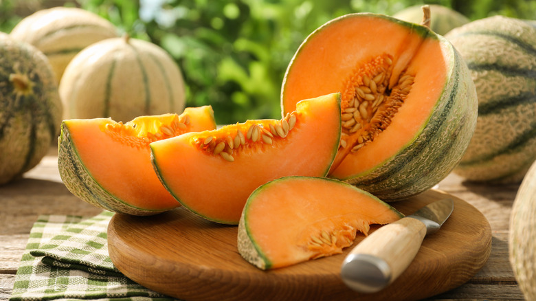sliced cantaloupe on wooden cutting with knife
