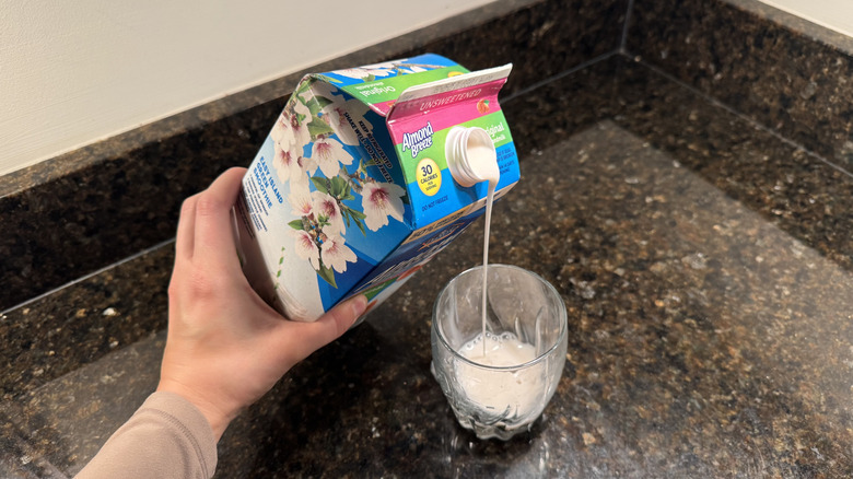 Person pouring a carton of almond milk into a glass