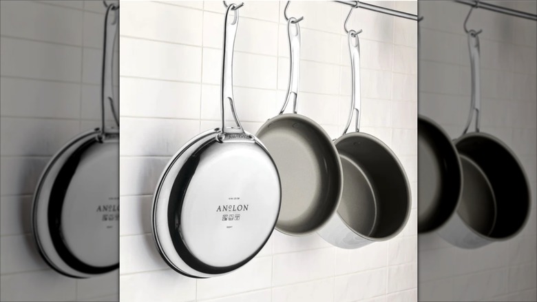 three Anolon pans hanging up in the kitchen against a white tile wall