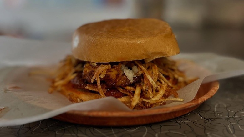 El Rey De Las Fritas frita dulce burger on parchment paper on a thin wooden plate.