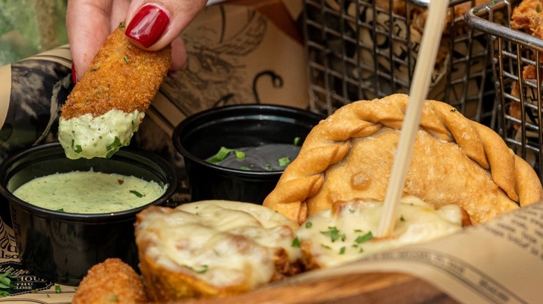 A person dipping a croqueta beside empanadas and tostones into a mojo rojo sauce at Sala'o.