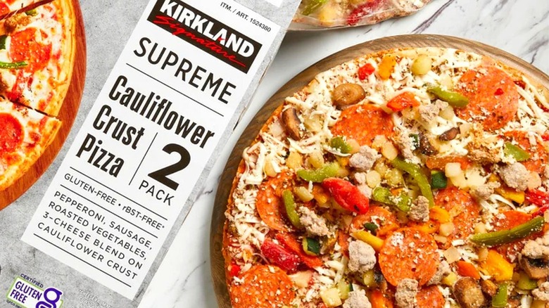 a close up picture of a Kirkland cauliflower crust pizza box alongside a pizza on a marble counter top
