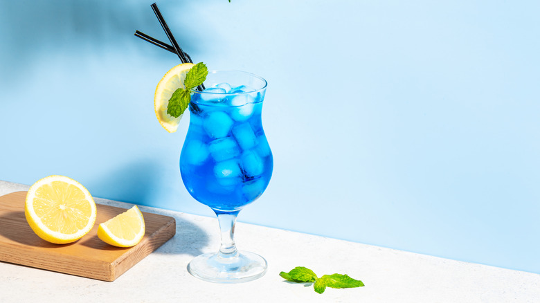 A tropical cocktail made with blue Curacao sitting next to a cutting board with sliced lemon