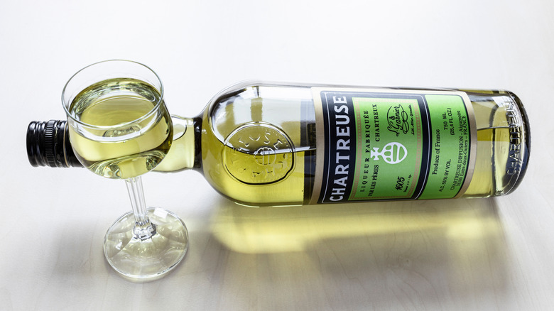 A bottle of green Chartreuse lying on its side with a snifter full of it